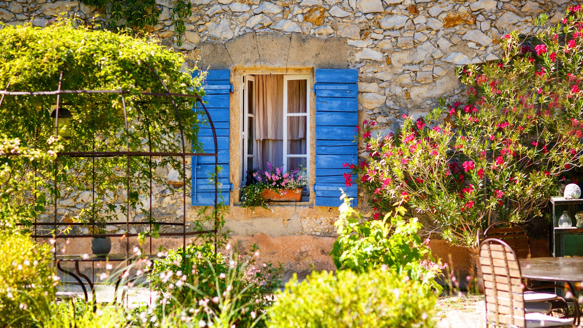 Fenêtre à volets bleus d'une maison en pierre provençale et son jardin fleuri